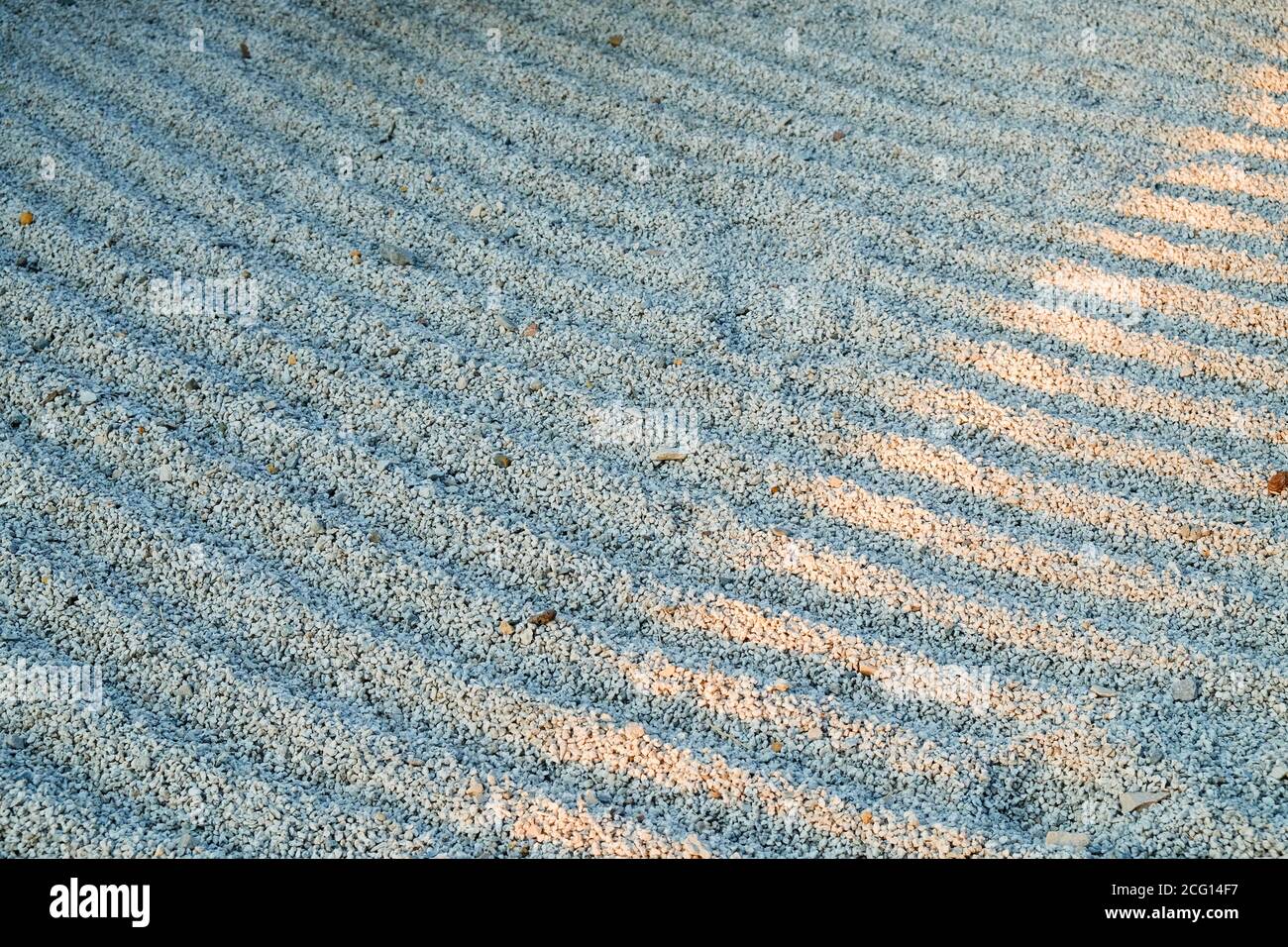 Sunshine ray on surface of gravel grooves symbolic rows in Gravel Stones Garden. Concentric lines of raked up white gravel in Japanese Zen Garden. Stock Photo