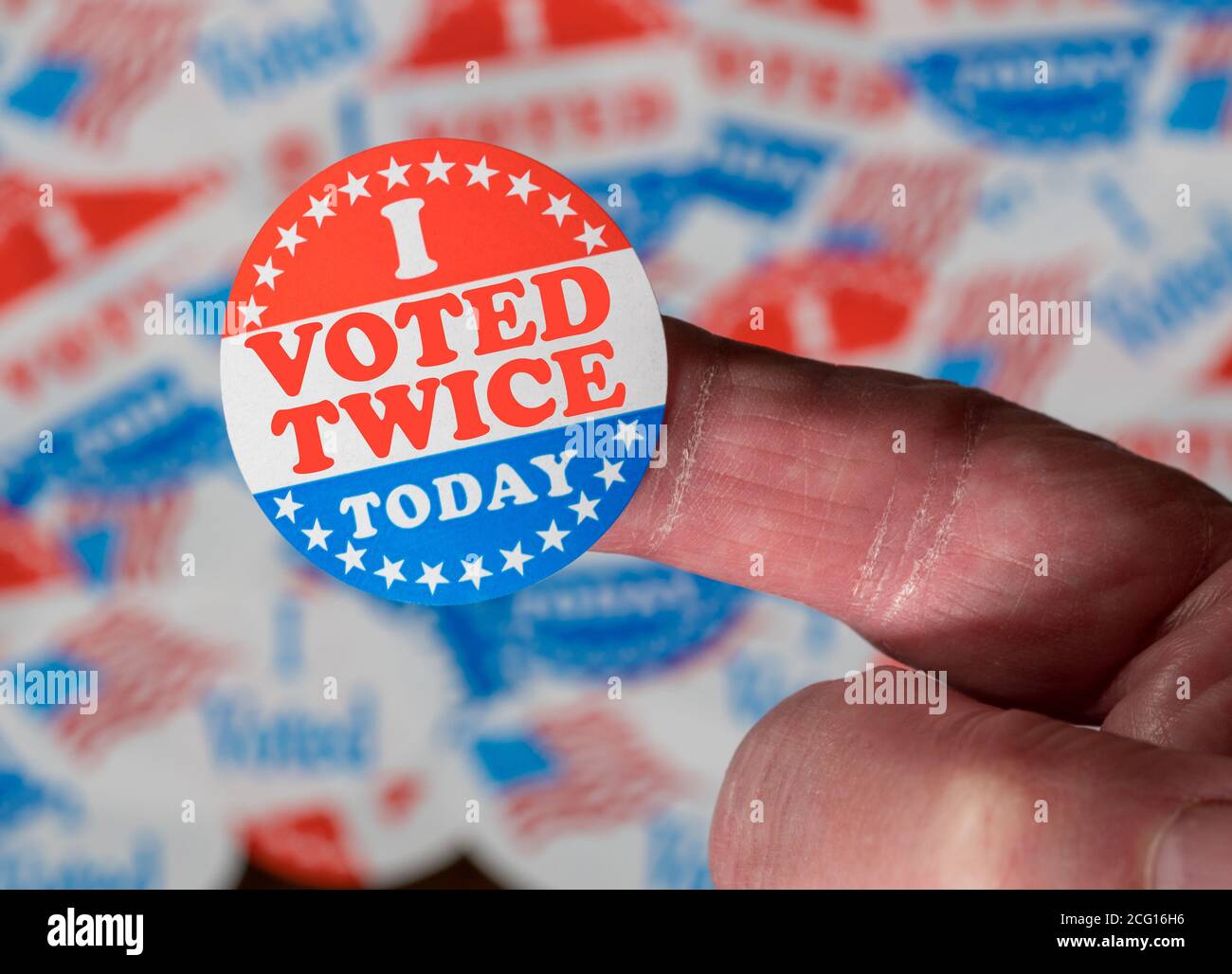 Finger with I Voted Twice button in front of many stickers given to US voters in Presidential election to illustrate vote fraud Stock Photo