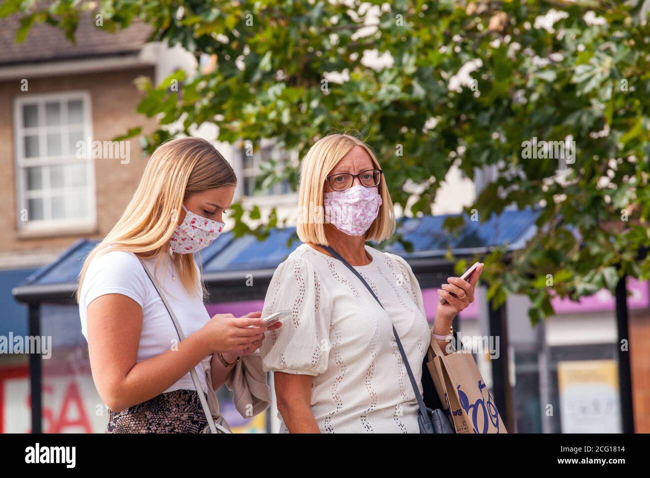 Two women wearing matching face mask covering using mobile phones during the Covid 19 pandemic Stock Photo
