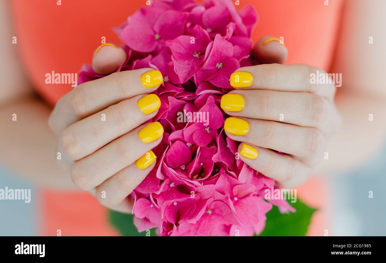 Women with manicured nails in yellow holding a flower Stock Photo