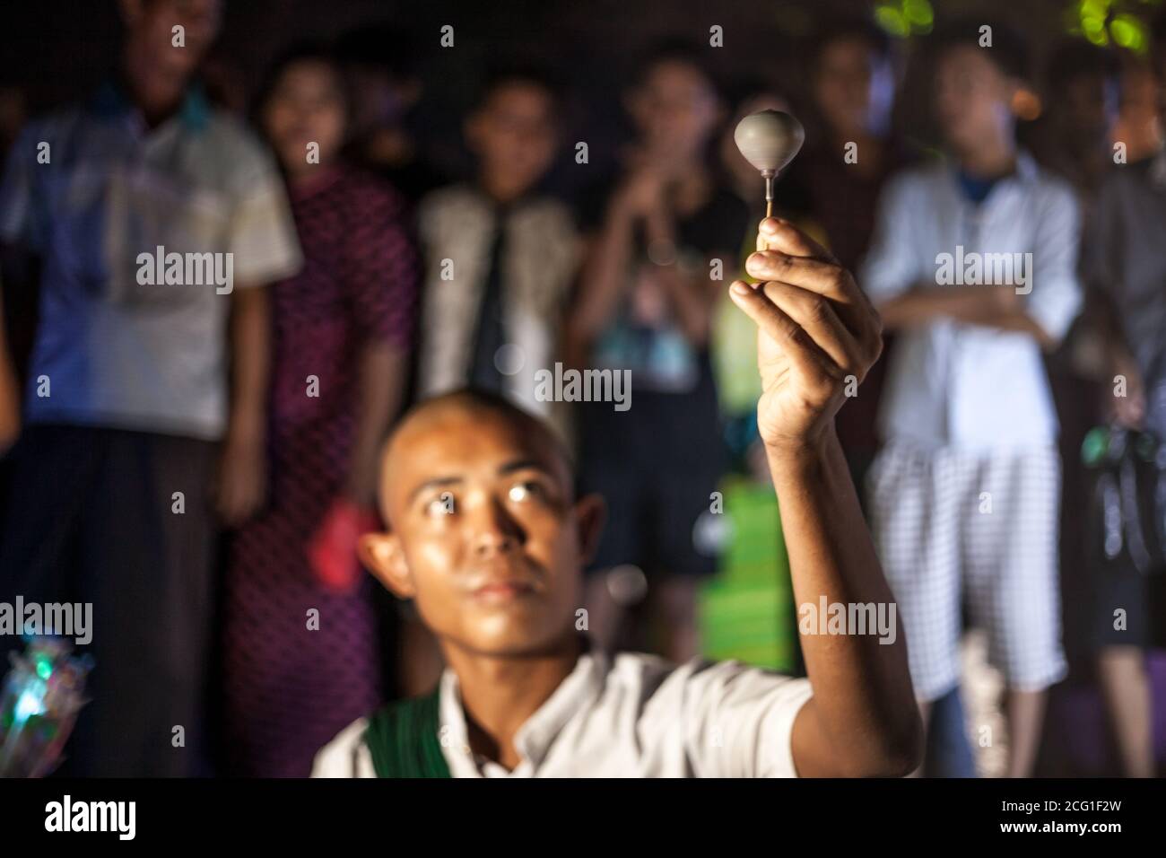 YANGON, MYANMAR DECEMBER 3, 2016 : Street performer in Maha Bandula Park with spinning top performs for crowd at night. Stock Photo