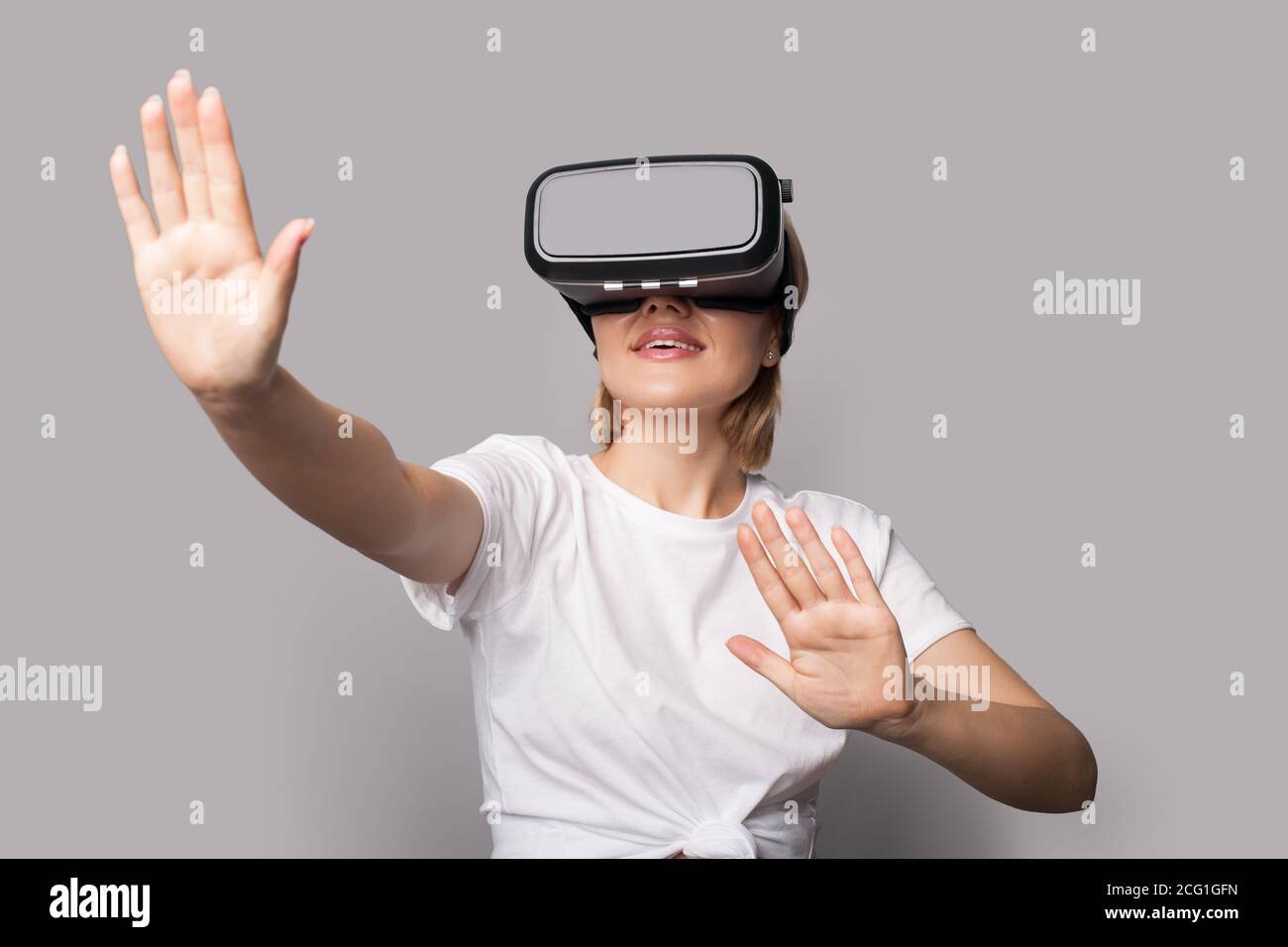 blonde woman with vr headset is touching something and posing on a grey  studio wall smiling Stock Photo - Alamy