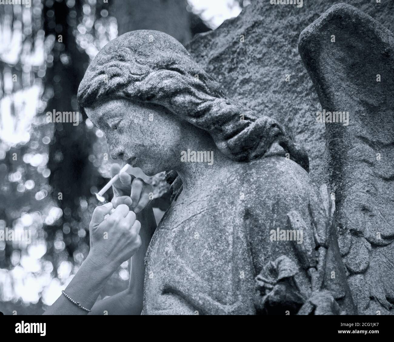 A close-up view of a woman lighting a cigarette for a cemetery angel statue Stock Photo