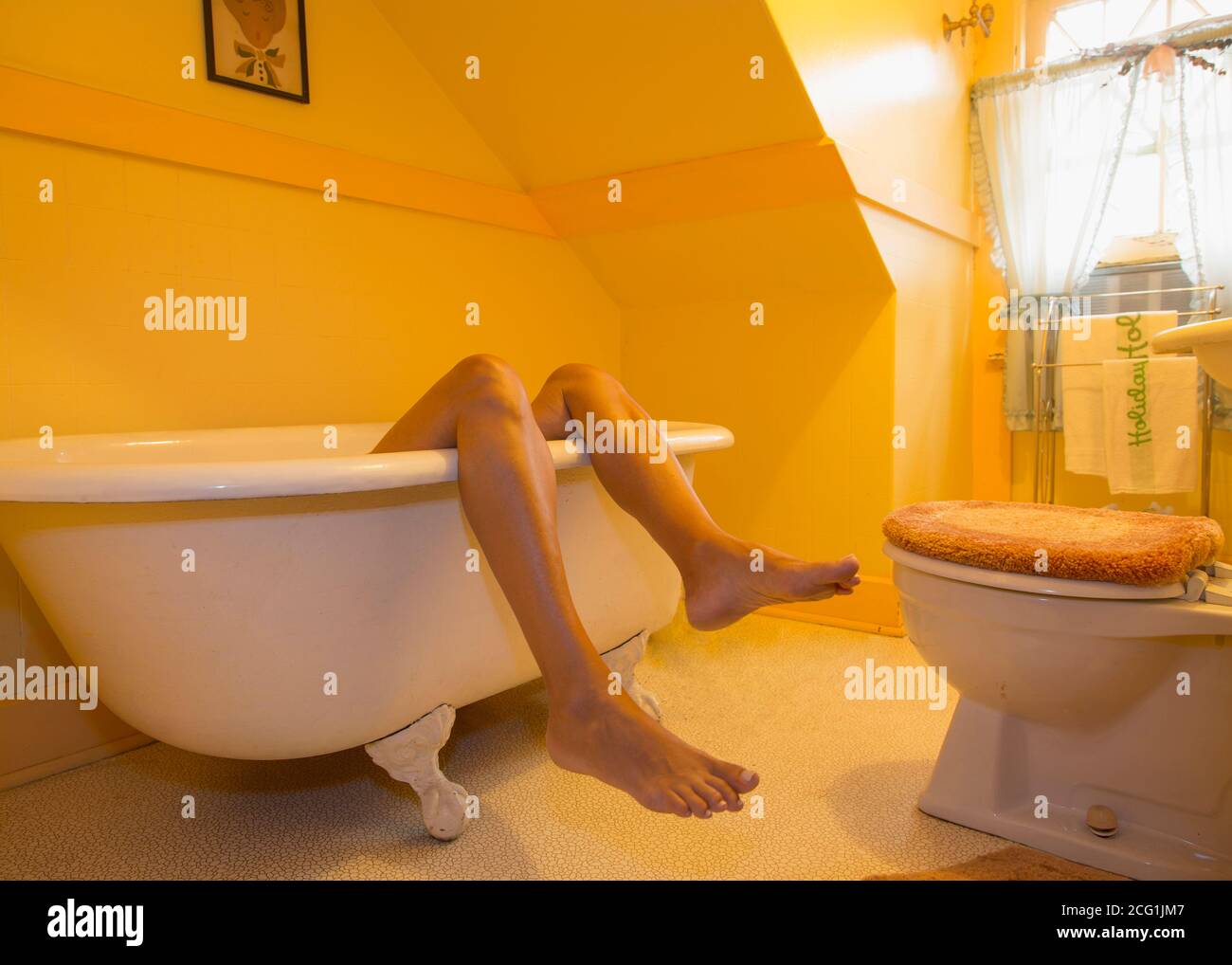 A woman's legs sticking out of a retro style claw-foot bathtub Stock Photo