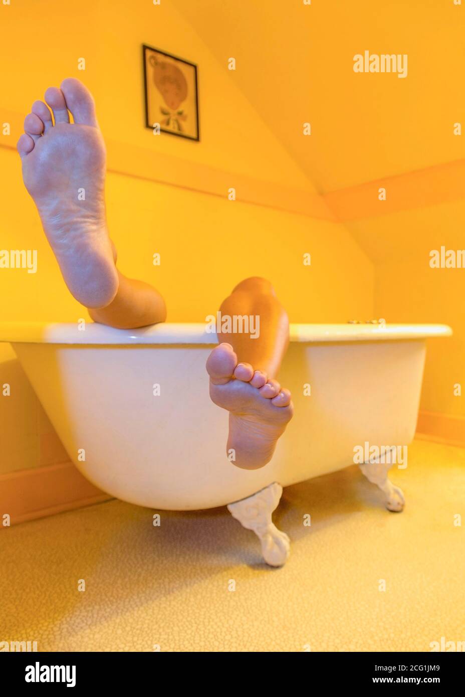Legs and feet sticking up out of a retro style claw-foot bathtub Stock Photo