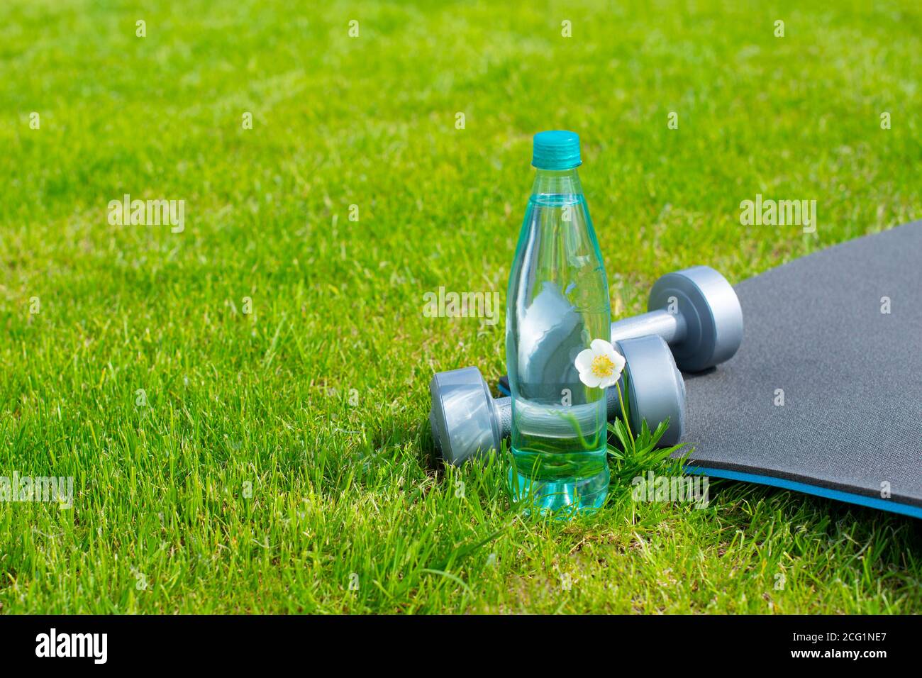 Bottle with water, dumbbells and a mat for sports and yoga on the green grass. Copy space Stock Photo