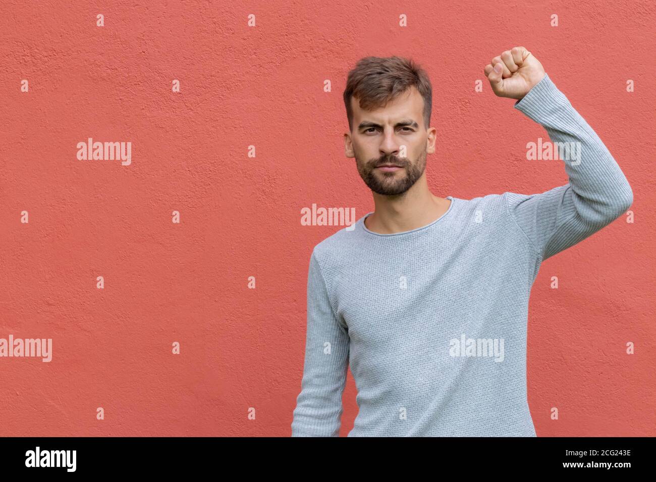 Determined guy raising up fist in air over red wall background. Young man demonstrating power. Protest concept. Stock Photo