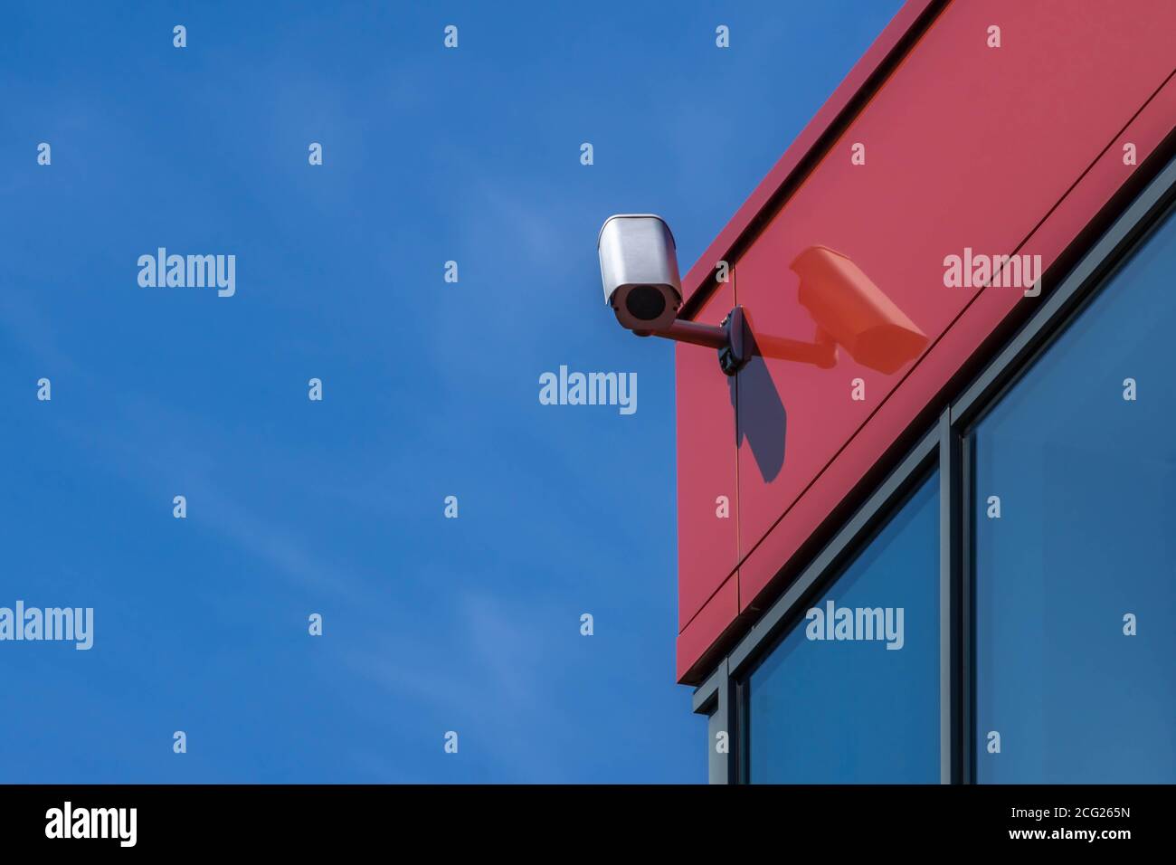 CCTV surveillance camera installed on modern red building wall. Security camera on blue sky background with copy space. Video equipment outdoor safety Stock Photo