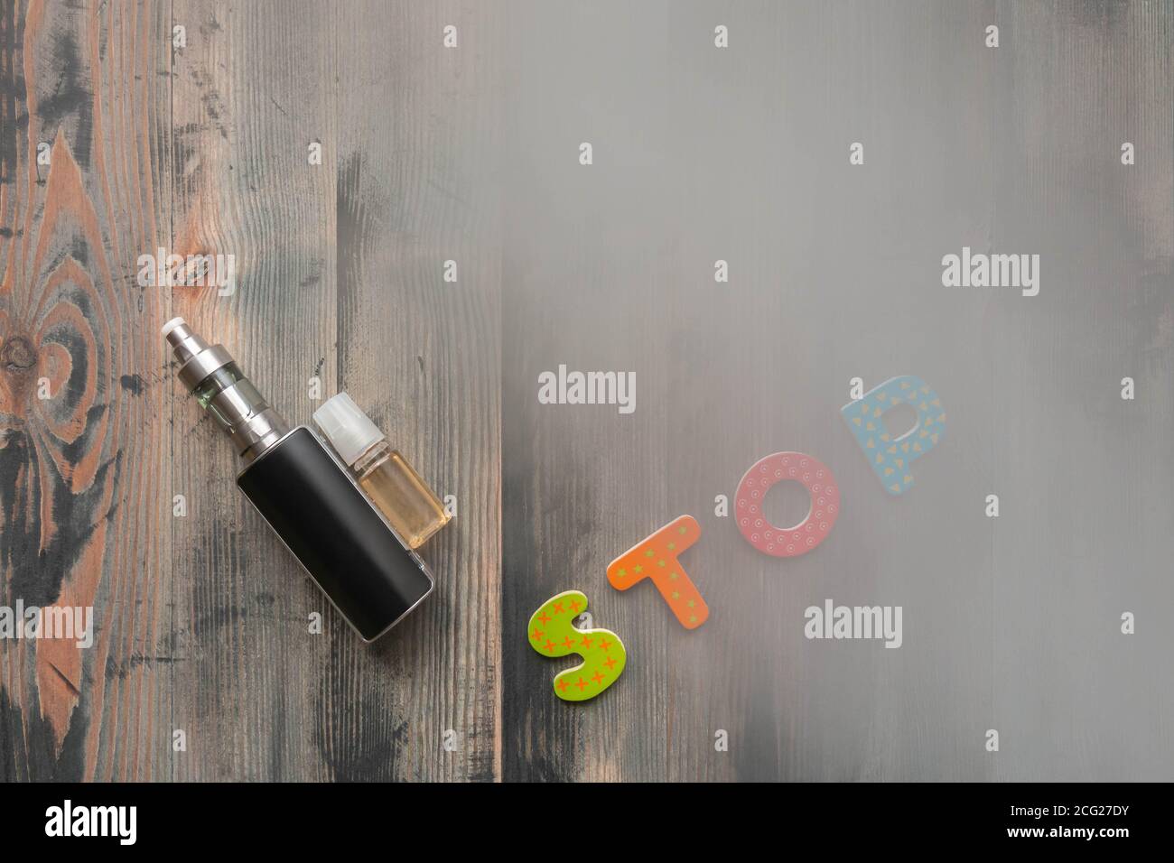 Black e-cigarette, sweet e-liquid, and word stop of wooden letters on grey wooden background covered smoke. Top view. Stop smoking concept Stock Photo