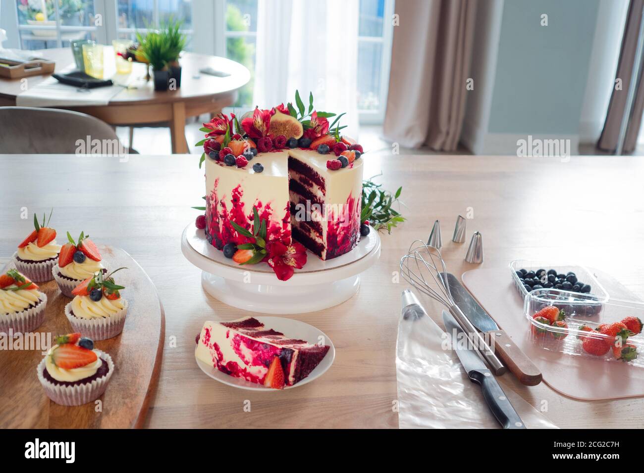 Big beautiful red velvet cake, with flowers and berries on top. Slice