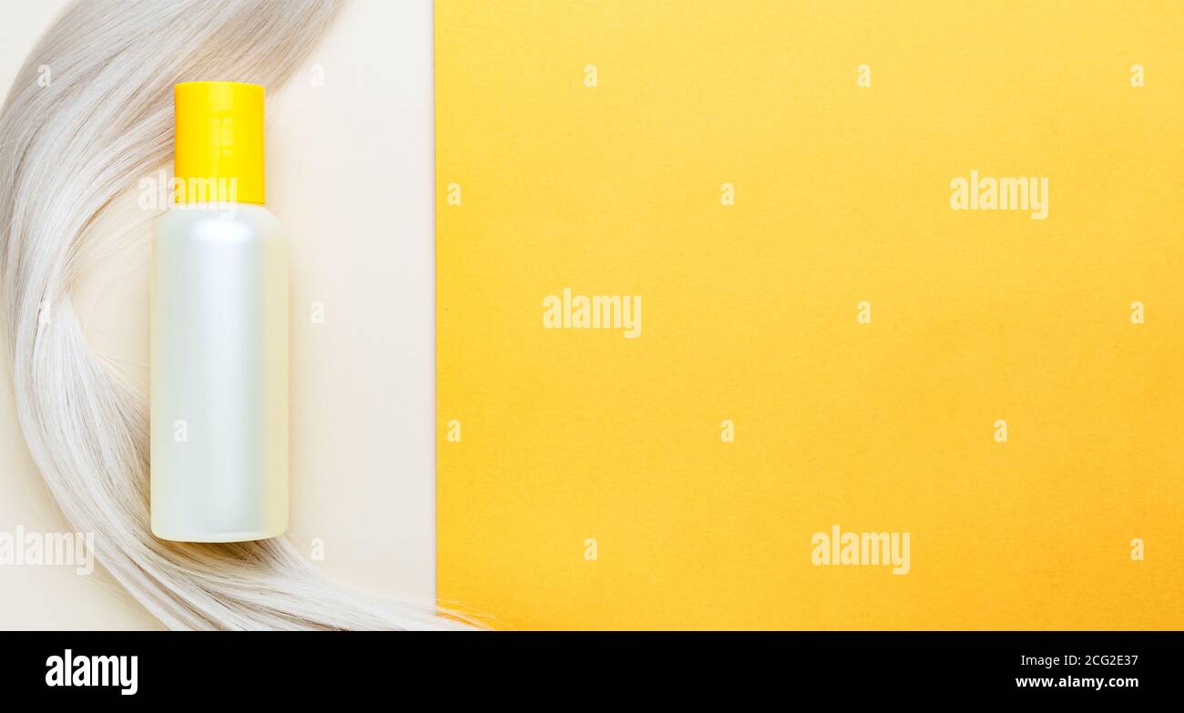 Shampoo bottle mockup strand on lock curl of blonde hair on orange color background. Yellow bottle shampoo. Web long bannner flat lay copy space.Hair Stock Photo
