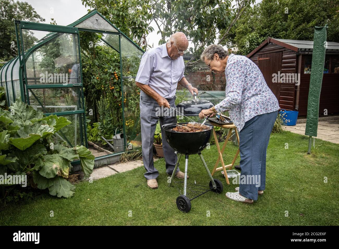 Retired couple in their 80's enjoying life outdoors barbecuing and eating healthy home grown vegetables during the coronavirus lockdown, Somerset, UK Stock Photo