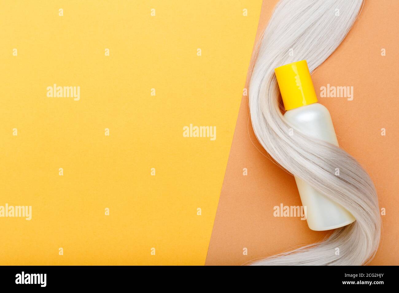 Shampoo bottle mockup strand on lock curl of blonde hair on orange color background. Yellow bottle shampoo. Flat lay copy space.Hair care cosmetics Stock Photo