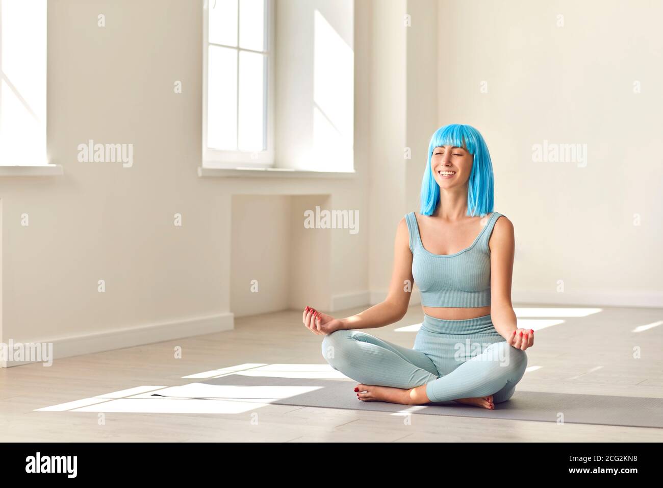Smiling young woman sitting in lotus position and meditating sitting on ...