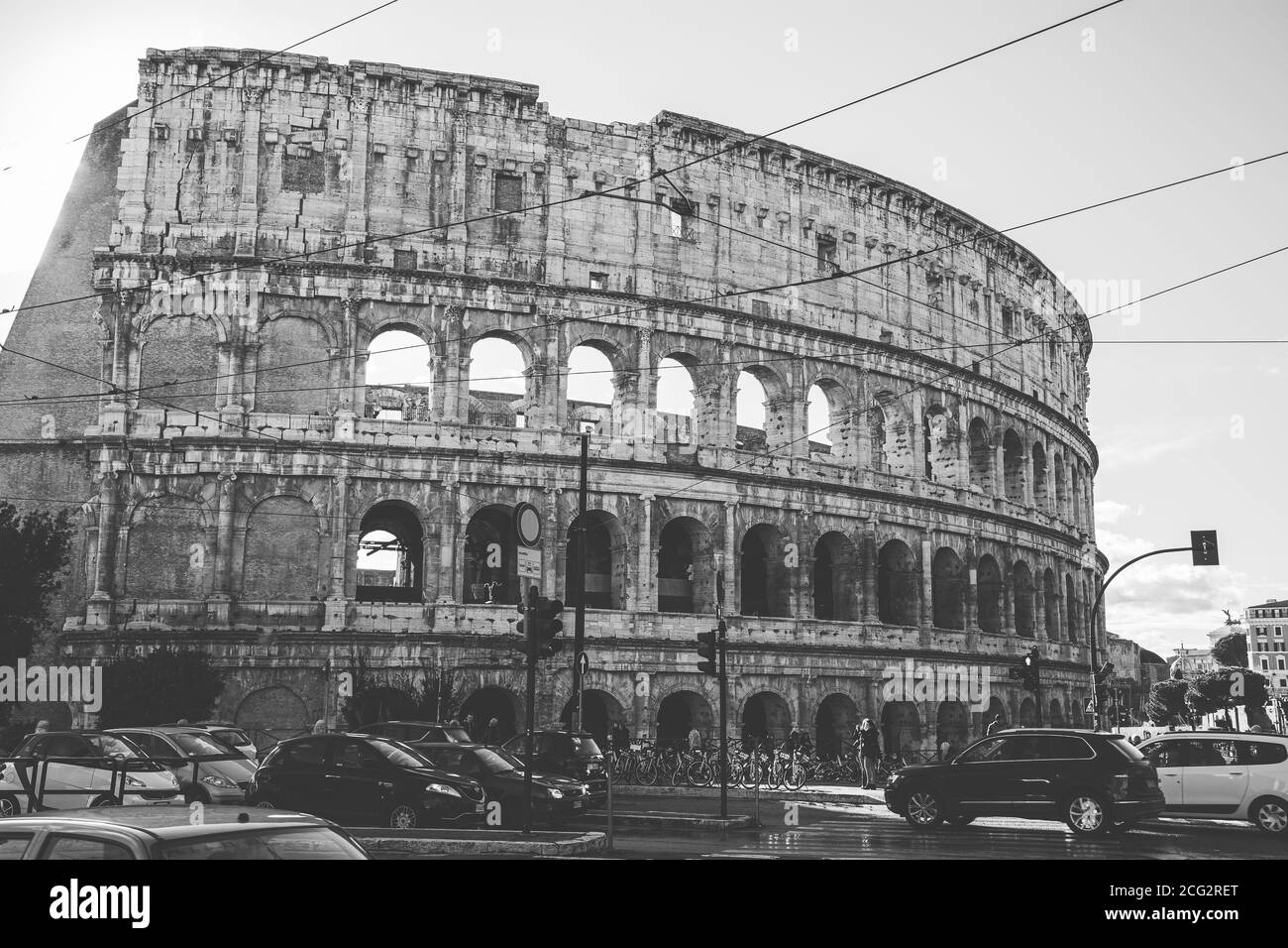 Black and white image of Colosseum against sky with traffic junction and cars in the foreground at Rome Stock Photo