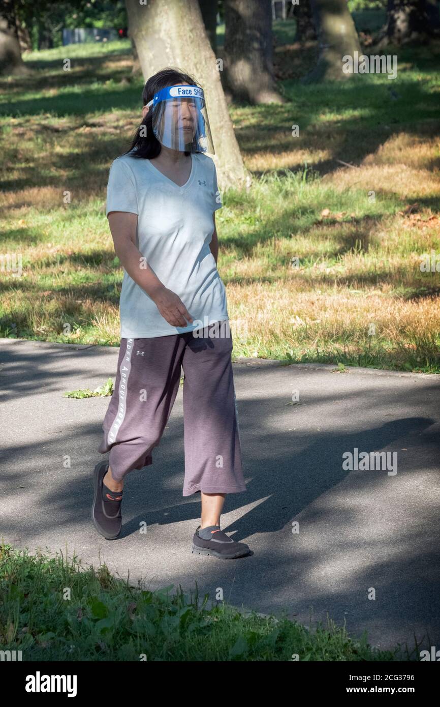 An Asian American woman out on an exercise walk wearing a face shield but no mask. I a park in Queens, New York City. Stock Photo