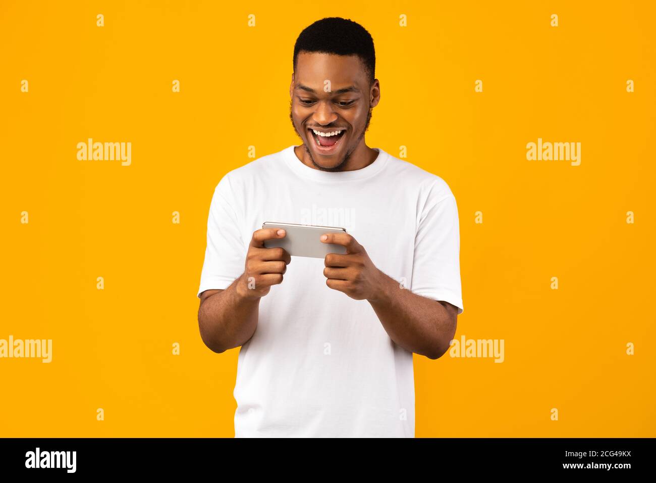 Excited Black Man Playing Games On Smartphone, Yellow Background Stock Photo