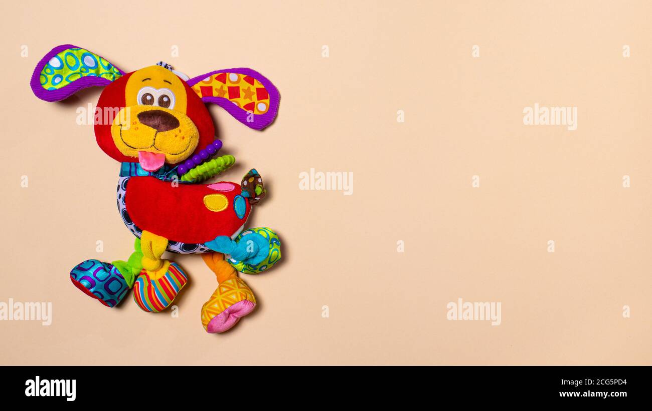 Red orange doggy toy on a beige background with room for text. Soft plush toy for baby dog banner for toy store. Stock Photo