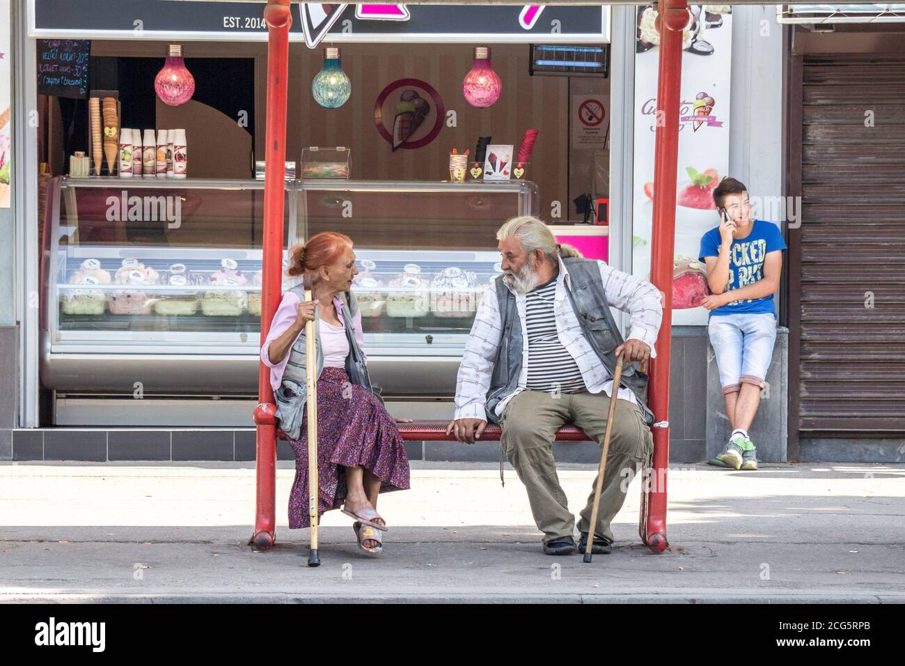PANCEVO, SERBIA - JUNE 13, 2015: Two old persons, a senior man and a woman, belonging to the roma community discussing while waiting a bus in the cent Stock Photo
