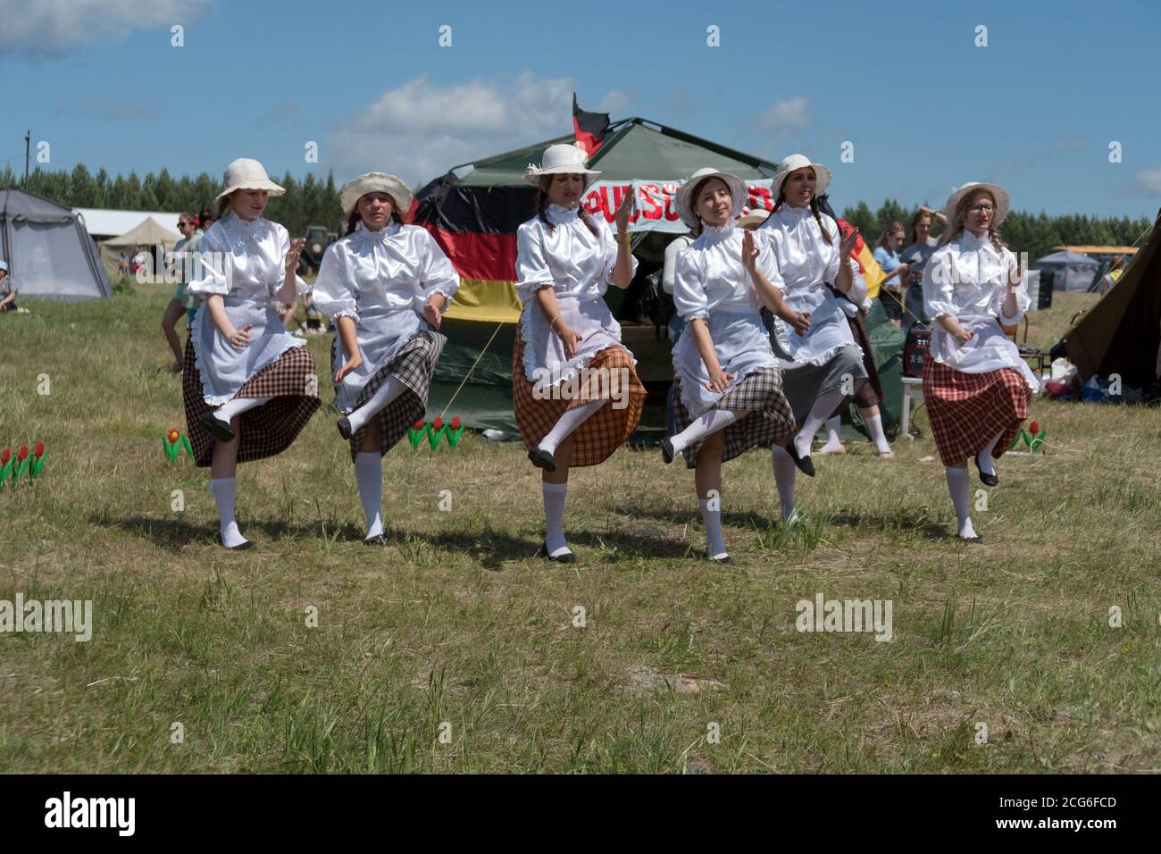 Girls dressed as German Frau dancing on the grass  during the ethnic festival Karatag on the shore of a Large lake. Stock Photo