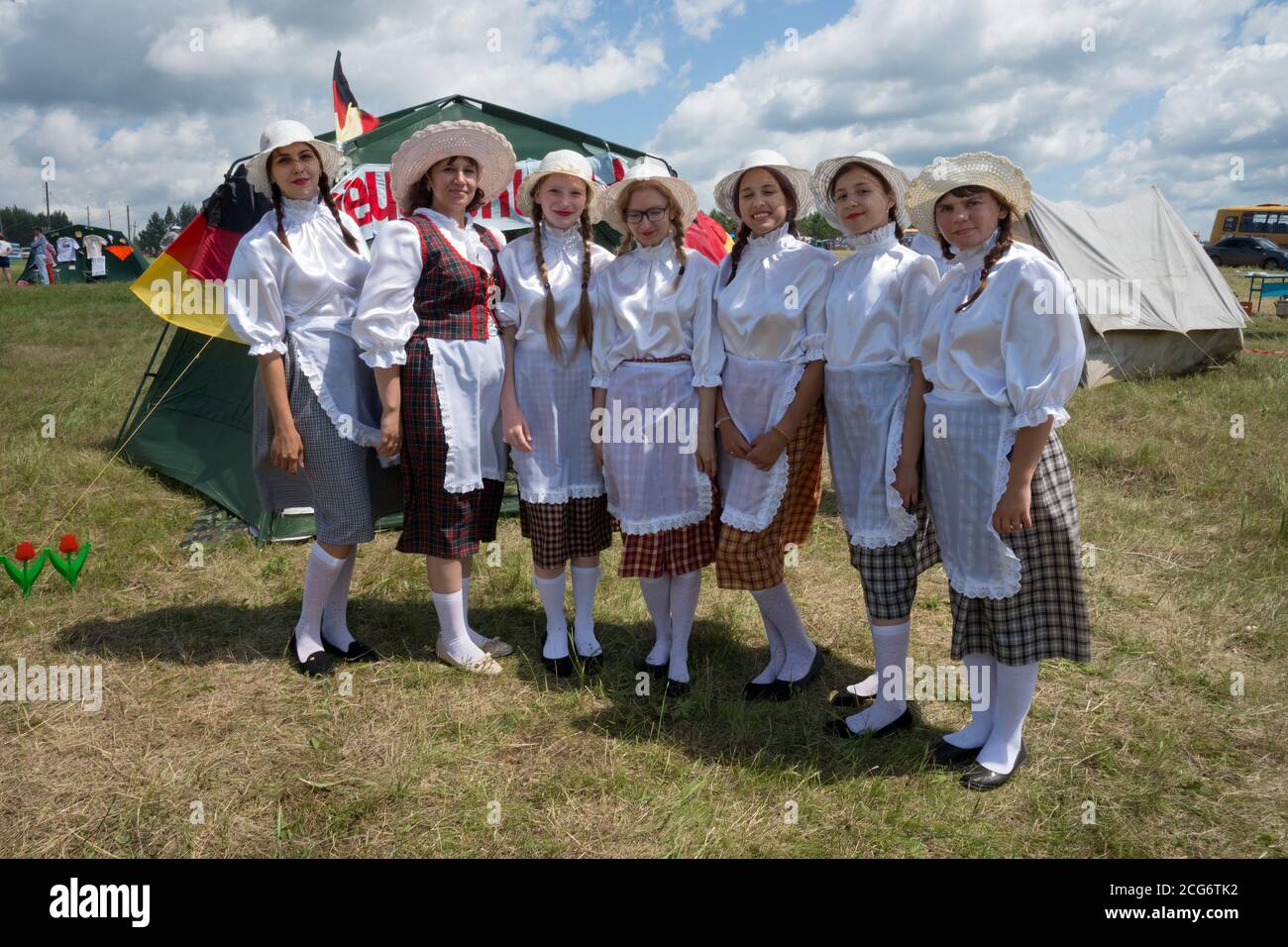 Girls in German Frau costumes stand in a clearing in the background of tents during the Karatag music festival. Krasnoyarsk region. Russia. Stock Photo