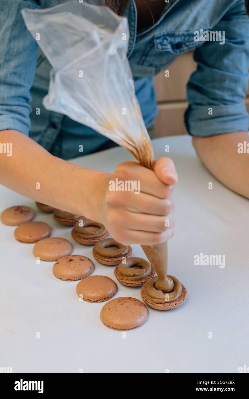 Woman filling chocolate macaroons with chocolate ganache Stock Photo
