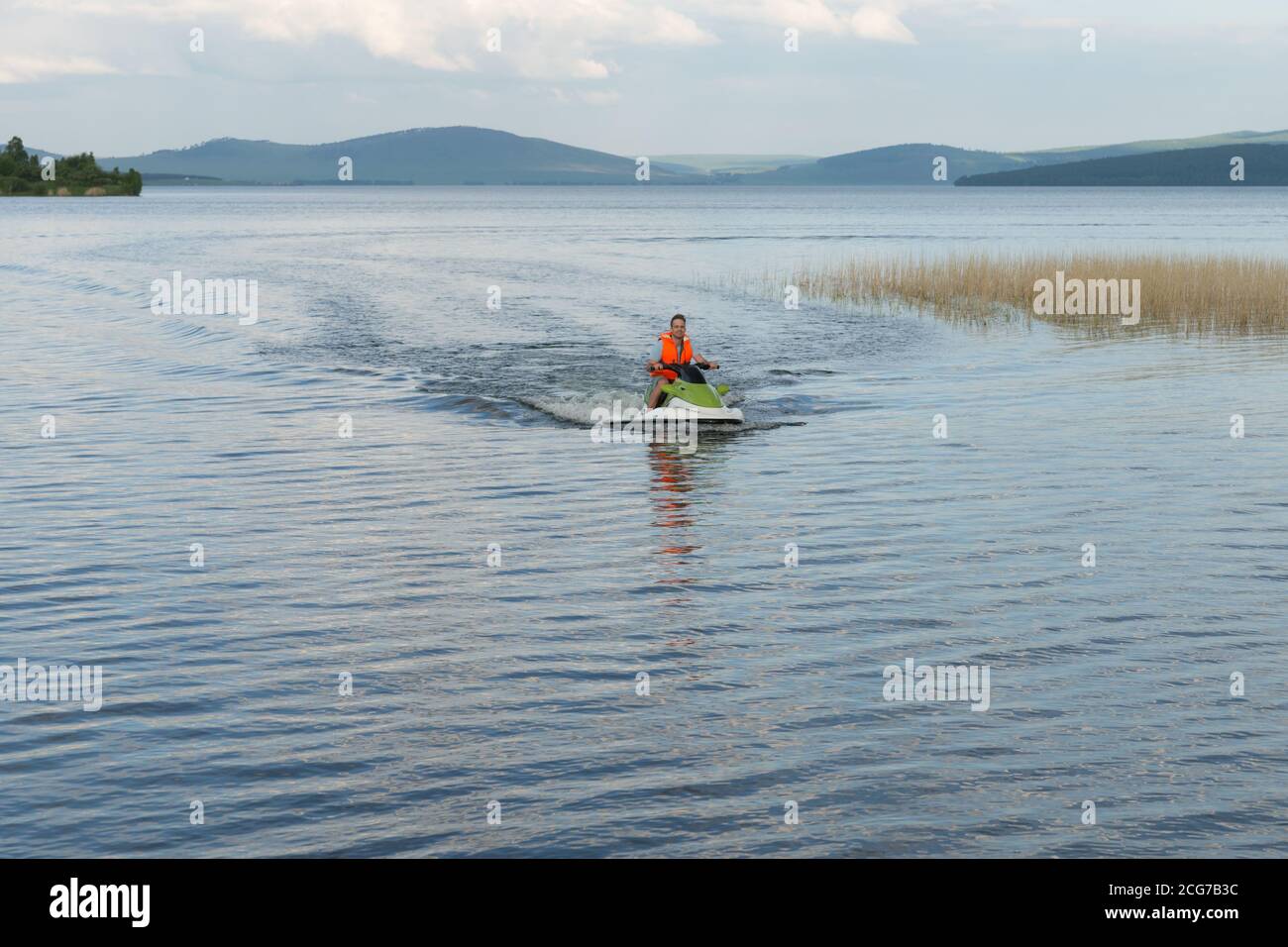 A young man in a life jacket rides a water bike on a lake in summer