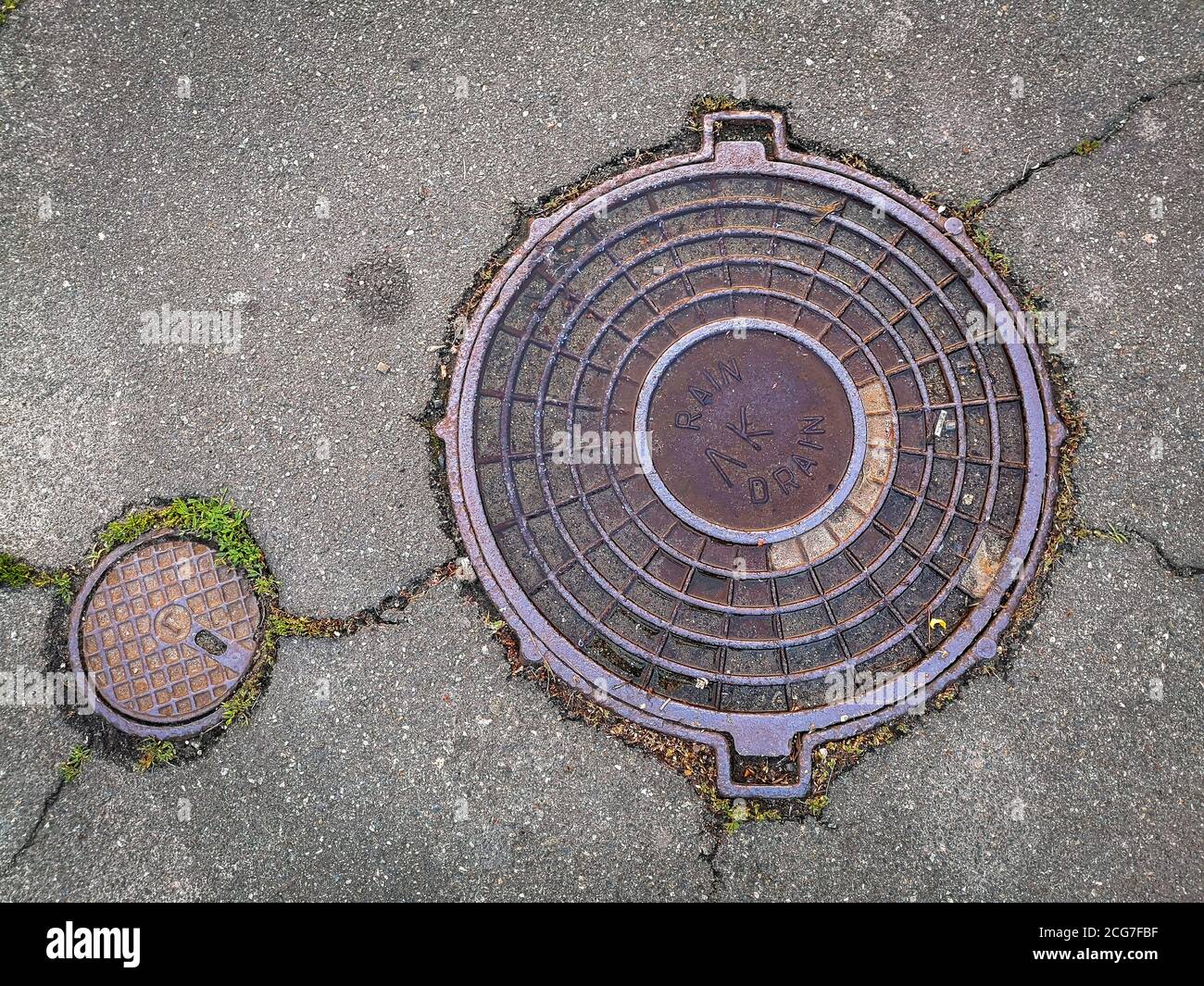 Top view of two circle manhole covers. Steel drain lids in a cracked asphalt. Stock Photo