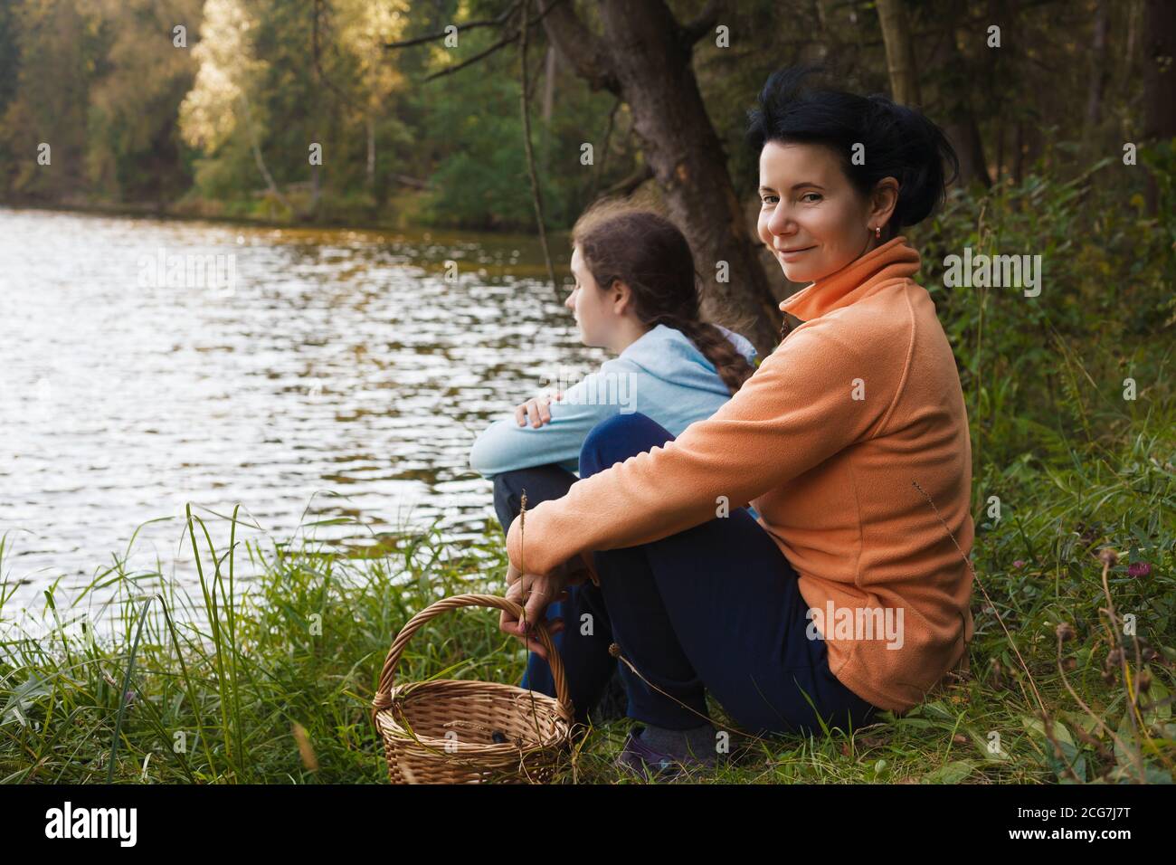 Family picnic during hiking. Mother and daughter sitting on a lake shore in a forest. Family concept. Stock Photo