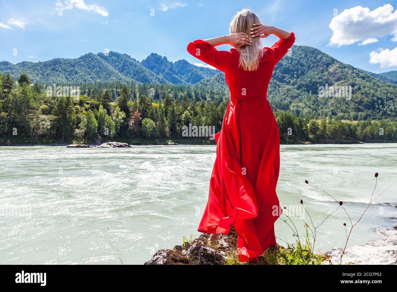 Back view of a blonde woman in a long red dress with her hands thrown back  behind her head against the background of the river, mountains covered with  Stock Photo - Alamy