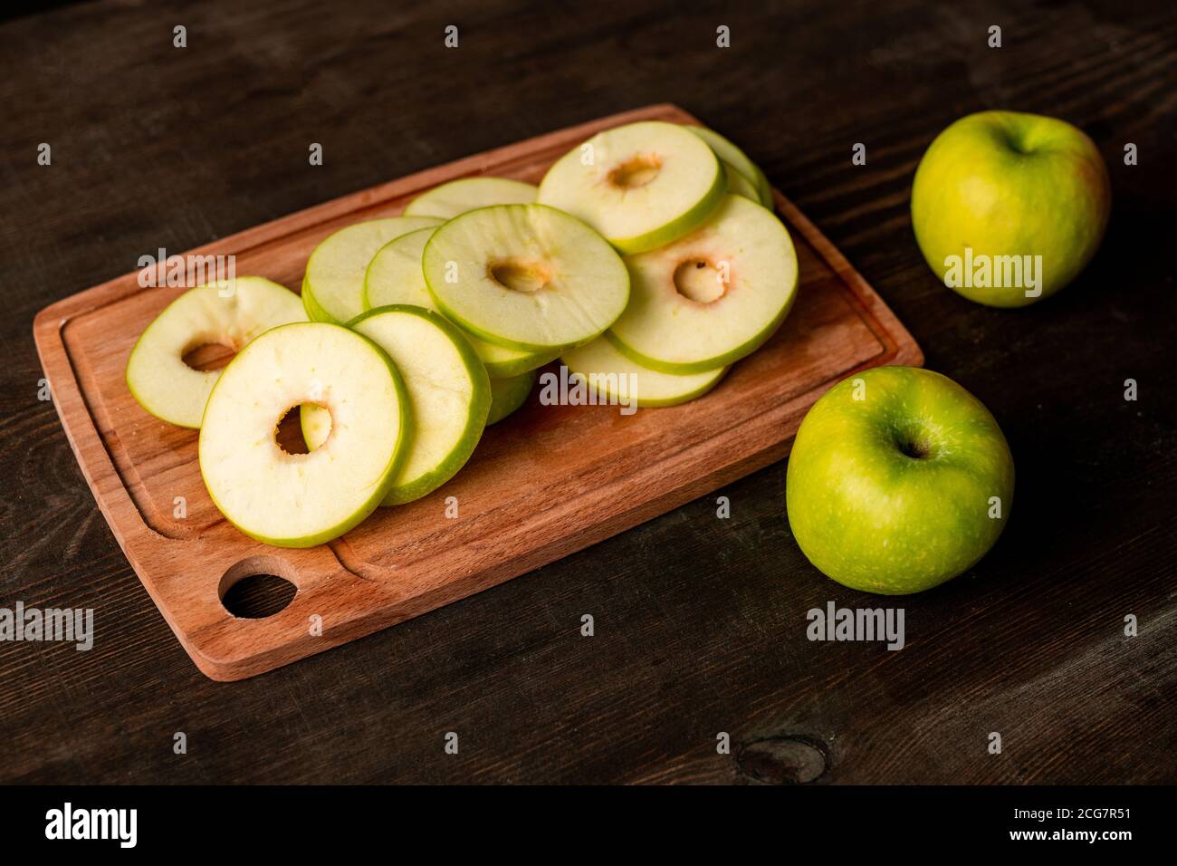 Close-up of green apple slices on cutting board and ripe apples on kitchen table, cooking concept Stock Photo