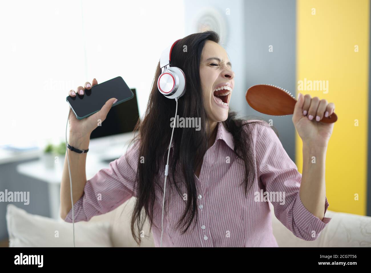 Woman with headphones and comb in her hands sings emotionally Stock Photo