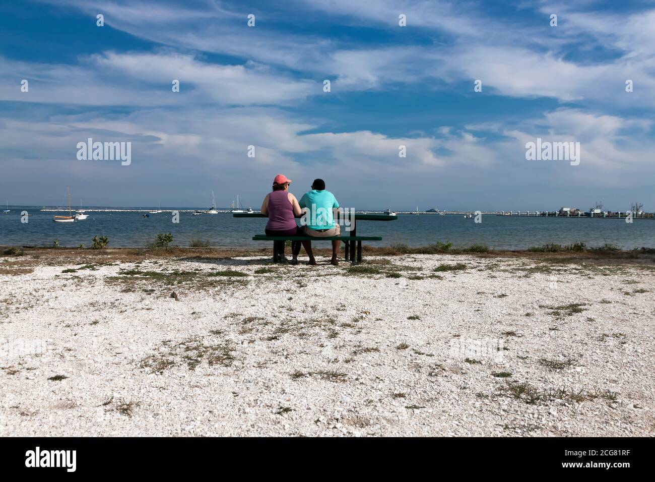 Multi-racial couple, in their forties, sitting & looking out at the water. Stock Photo
