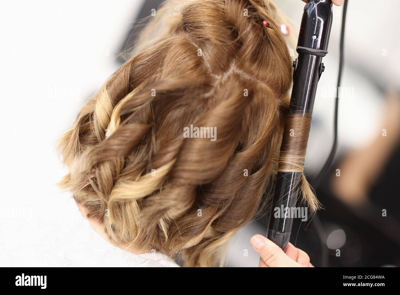 Hairdresser makes curls on women's hair with curling iron Stock Photo
