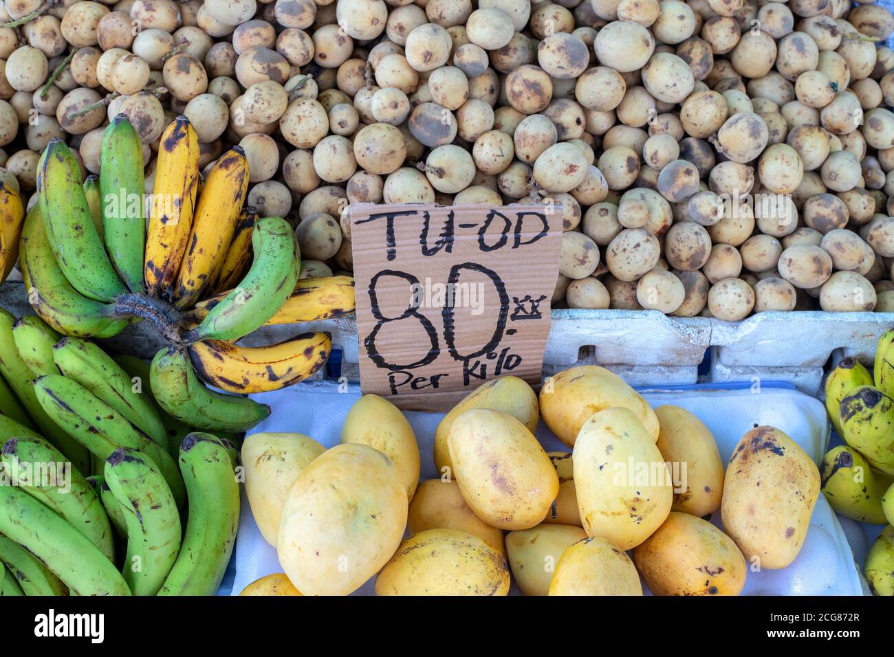 Mango, langsat and banana on farm market. Price tag with inscription Mango in cebuano language. Philippines farm market with tropical fruits on stall. Stock Photo