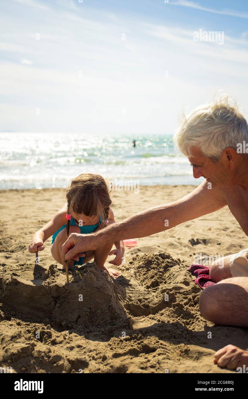Caucasian grandfather and granddaughter playing with sand, building a sand castle together on the beach. vertical shot. Stock Photo