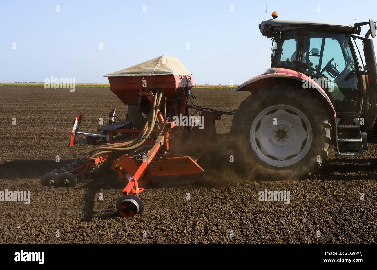 Farmer with tractor seeding crops in the field. Stock Photo