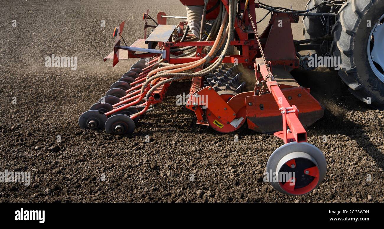 Farmer with tractor seeding crops in the field. Stock Photo