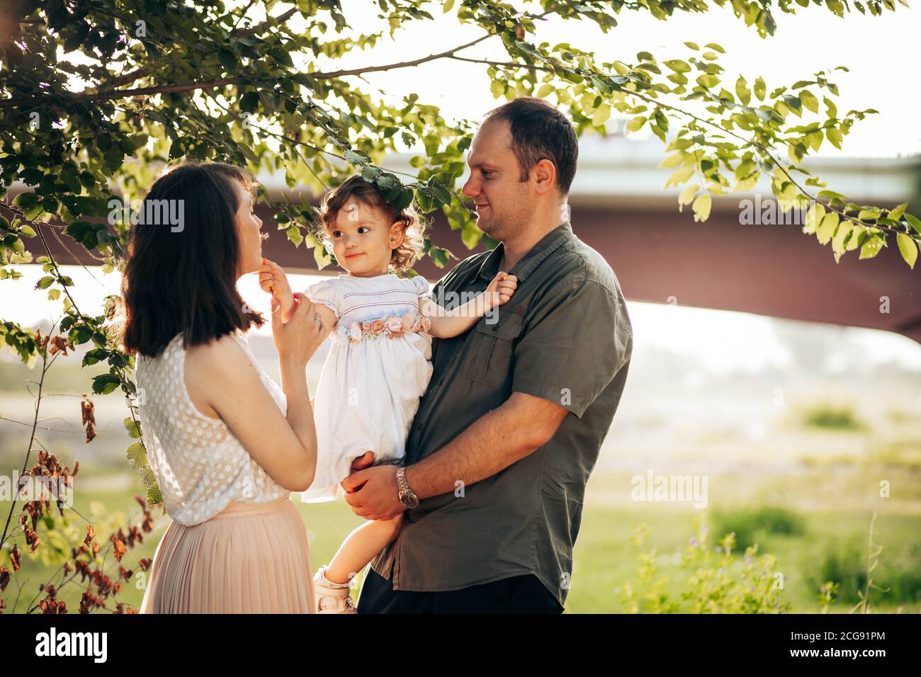 Happy family, mother, father and little daughter have fun outdoors. Dad holds his daughter in his arms Stock Photo