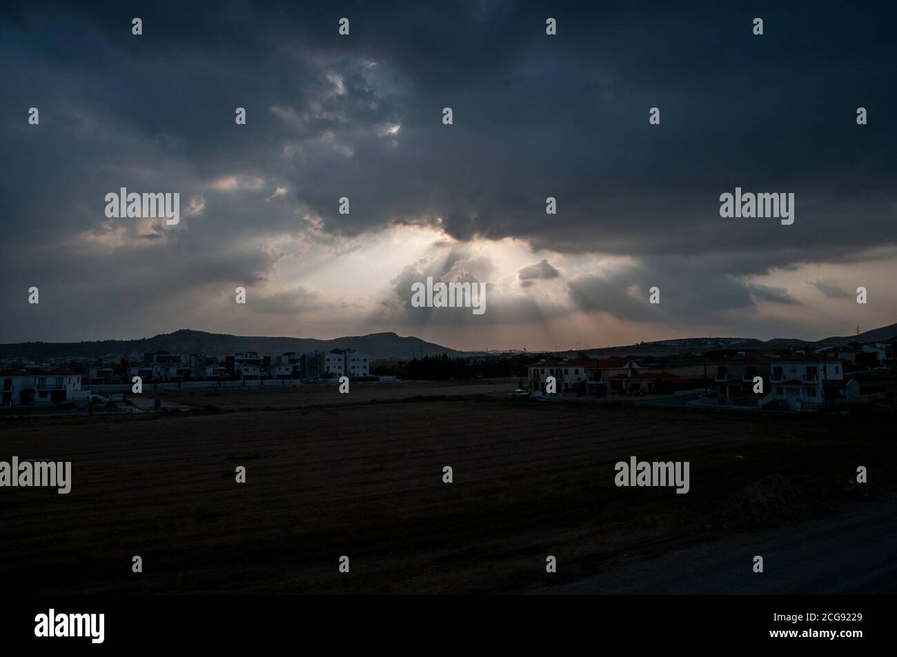 Rays of sunlight breaking through heavy clouds over silhouetted landscape of south eastern Cyprus. Stock Photo