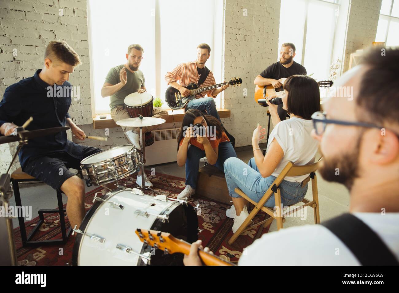 Songs. Musician band jamming together in art workplace with instruments. Caucasian men and women, musicians, playing and singing together. Concept of music, hobby, emotions, art occupation. Stock Photo