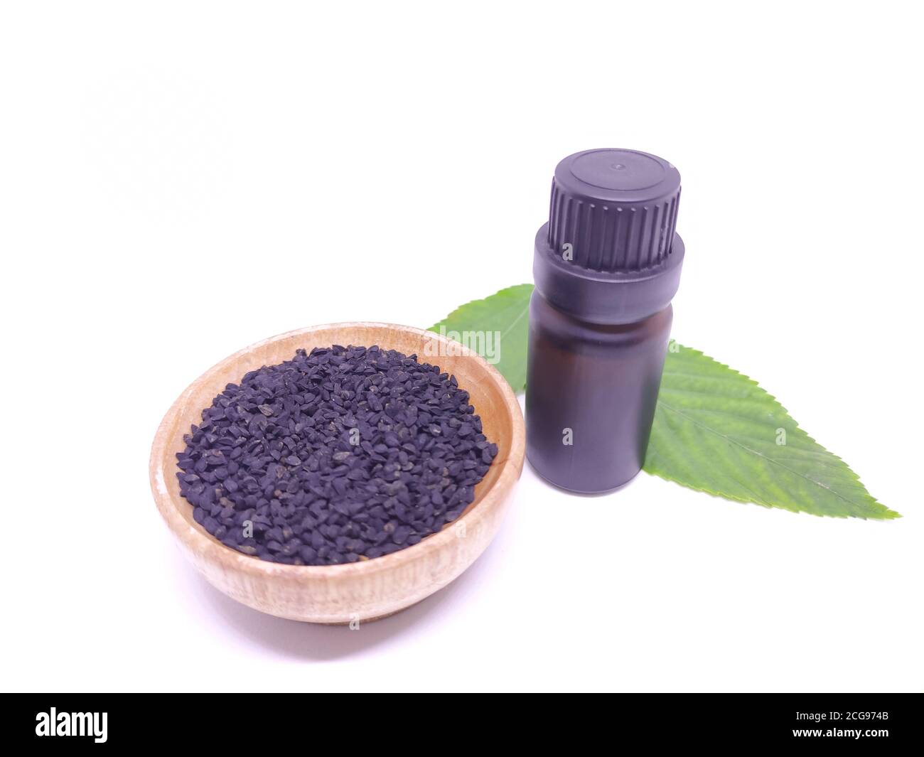Black cumin seeds in a wooden bowl and oil in a bottle with green leaves. Stock Photo