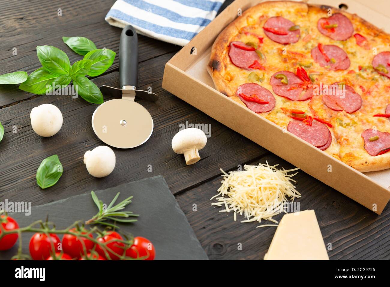 Tasty hot pizza with ingredients and pizza cutting knife on a black texture background Stock Photo