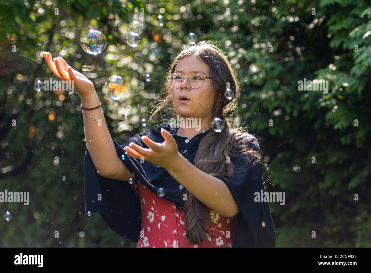 Closeup picture of a middle-aged, in her 50s, Asian woman with soap bubbles. Green leaves in the background Stock Photo