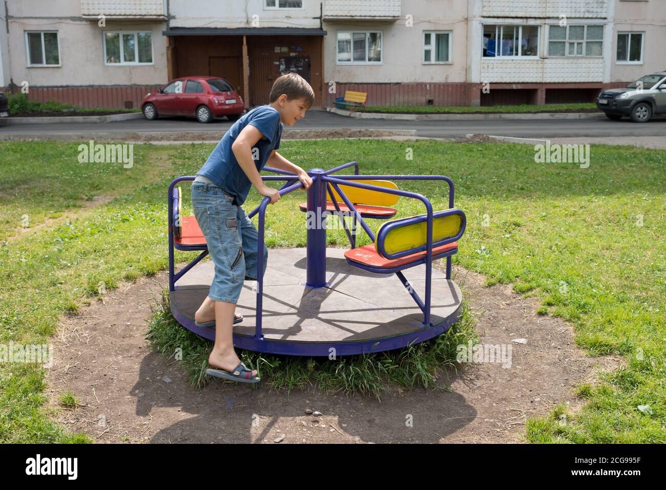The boy is spinning on a swing in the courtyard of a residential building. Stock Photo