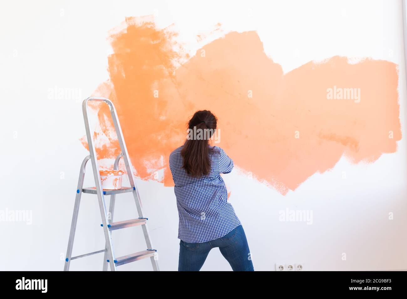 Dancing funny woman painting interior wall of home with paint roller