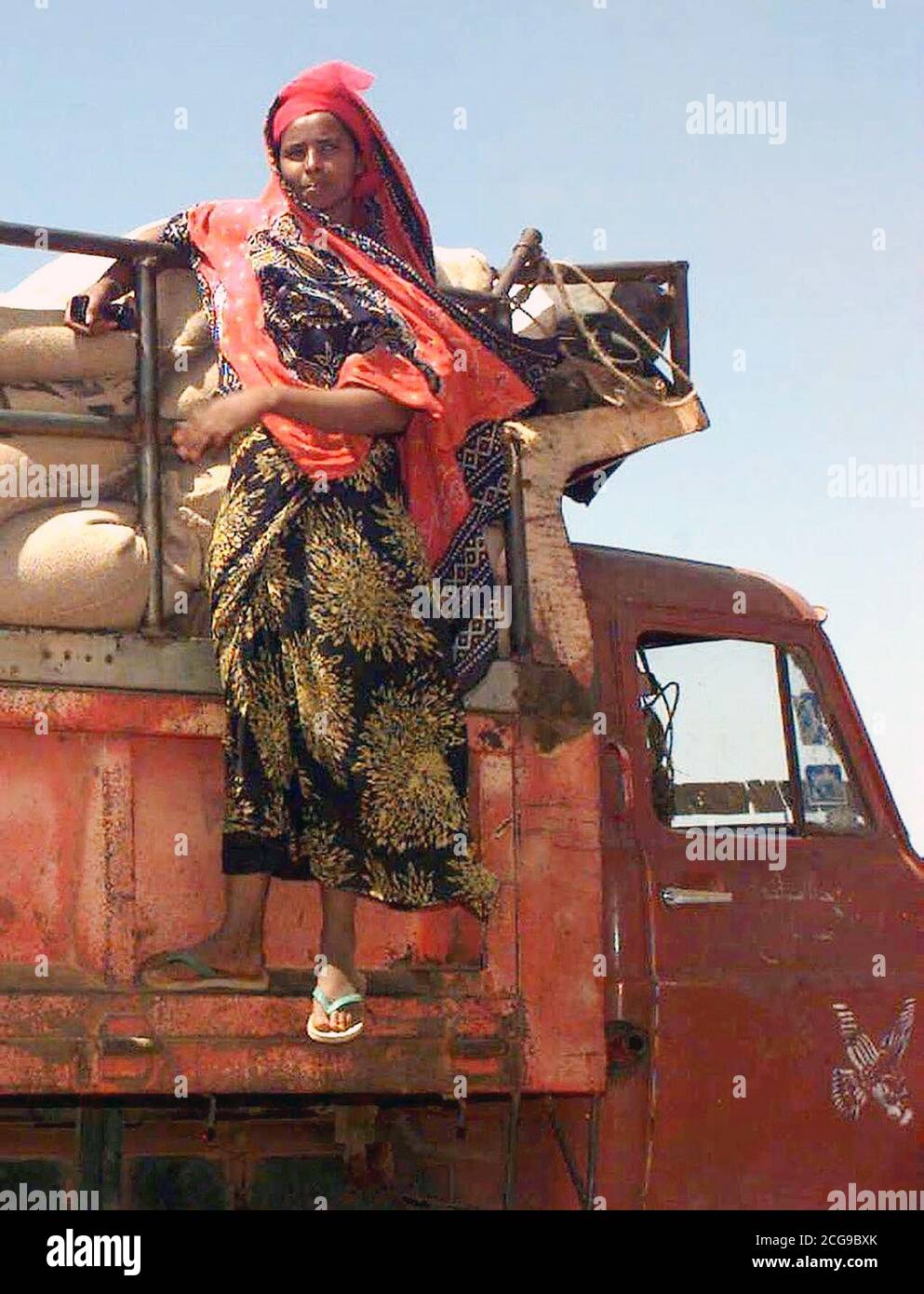 1993 - Straight on shot of a Somali Woman clinging to the right side of the dump rack on an Isuzu dump truck.  She watches the men load the bags of wheat donated by the people of Australia (not shown).  This mission is in direct support of Operation Restore Hope. Stock Photo