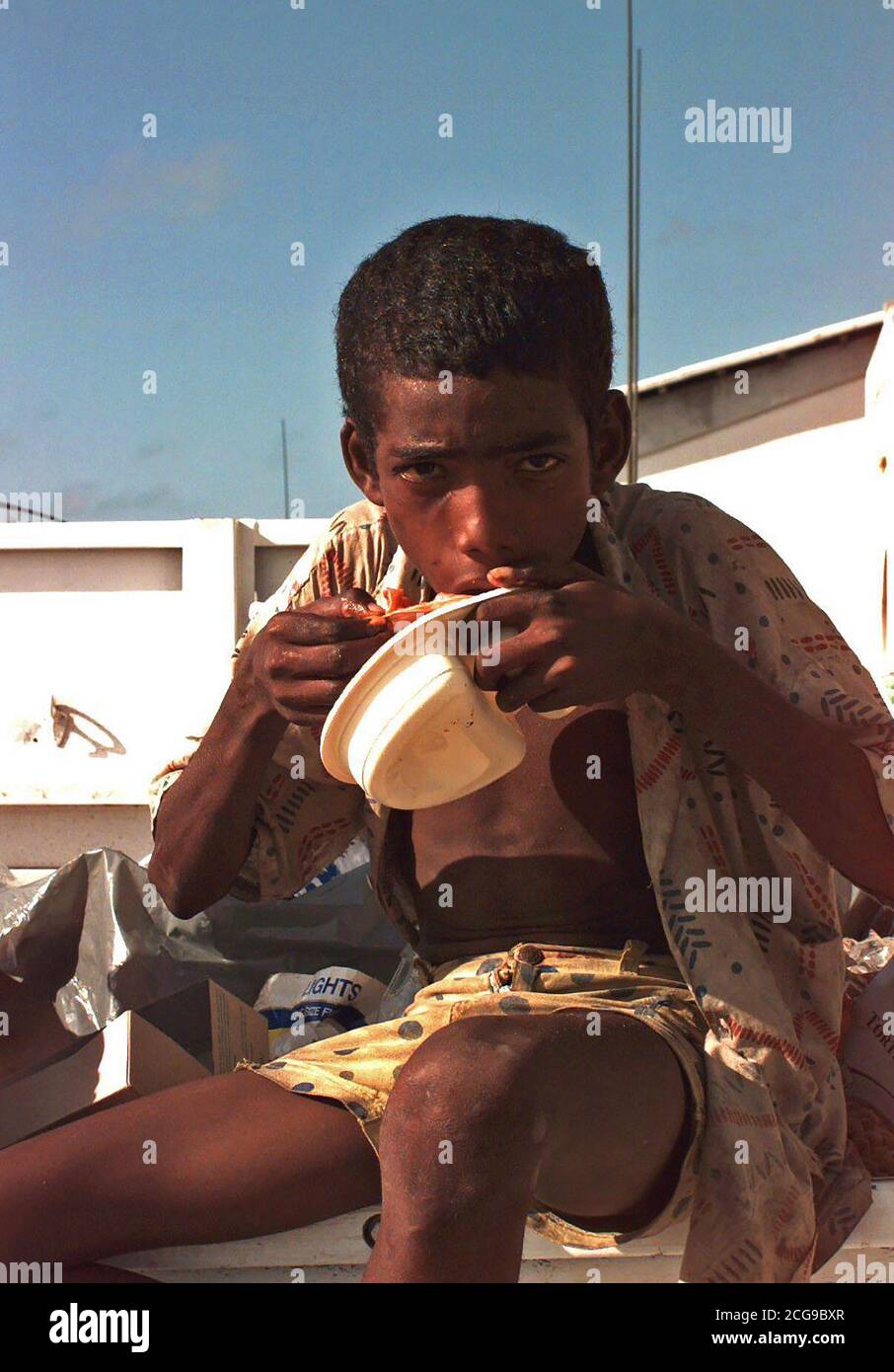 1992 - A young Somali finds discarded food in the trash at the Belgian Army compound. Stock Photo
