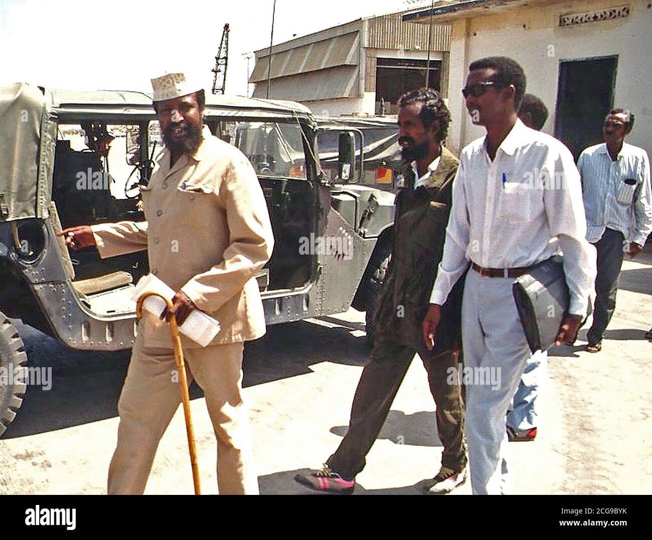 1992 - Straight on shot of Somali Faction Leader COL Jess, at left with hat and cane, walking outside the Joint Task Force Headquarters in Kismayo, Somalia with his entourage.  He had just completed a meeting with BGEN Lawson Magruder, USA, Joint Task Force Commander in Kismayo.  BGEN Magruder, (not shown) is from the 10th Mountain Division Fort Drum, New York.  This mission is in direct support of Operation Restore Hope. Stock Photo