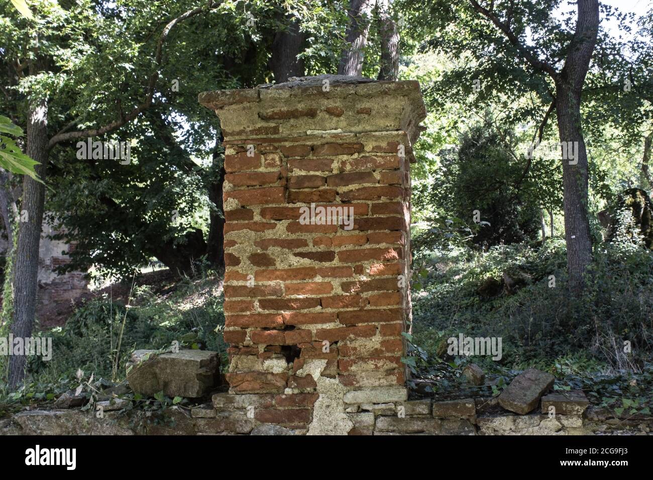 A brick fence post. Trees behind the brick wall. Stock Photo